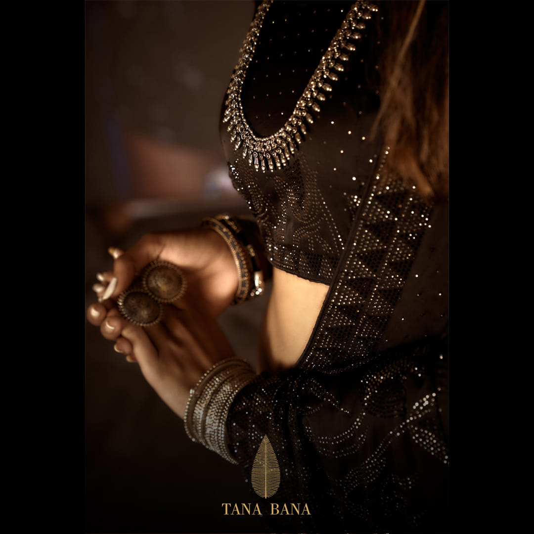 picture of woman's torso, left arm and hands. she is wearing a luxurious brown saree with swarovski crystals embedded on the sari. the model is set against a dark brown backdrop.